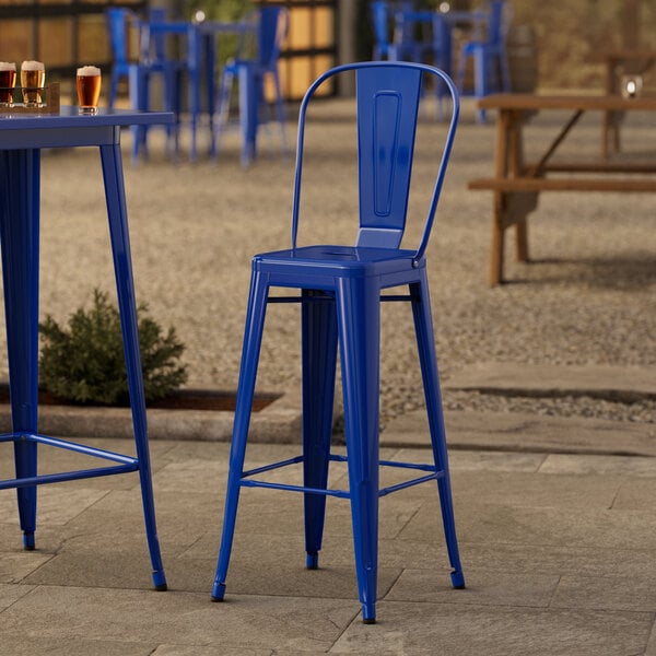 A blue metal Lancaster Table & Seating outdoor cafe barstool on a patio with beer glasses on the table.