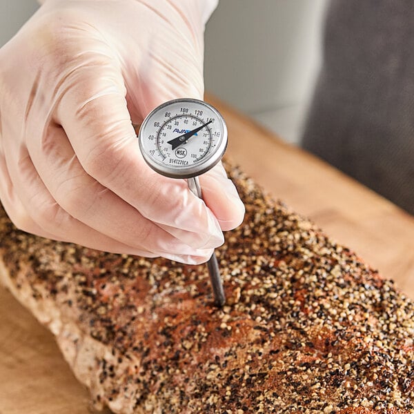 A pocket probe dial thermometer being used to check the temperature of a seasoned meat roast.