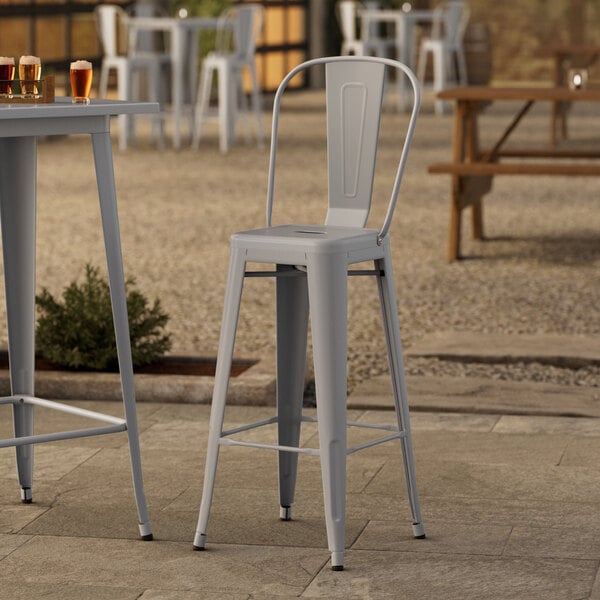 A Lancaster Table & Seating metal outdoor cafe bar stool on a patio.