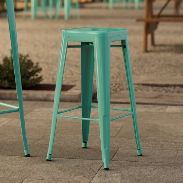 Two turquoise Lancaster Table & Seating outdoor barstools on a stone patio.