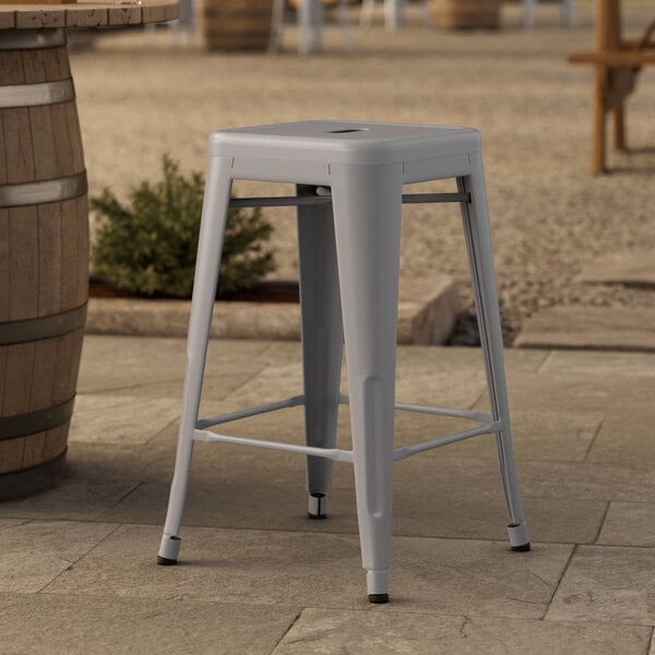 A Lancaster Table & Seating nickel gray metal outdoor counter height stool on a stone surface.