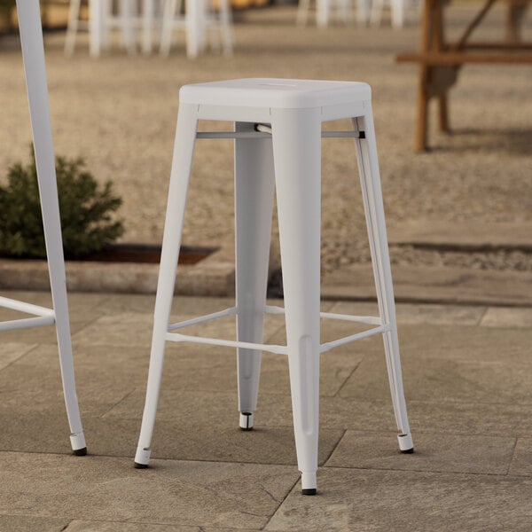 A white Lancaster Table & Seating outdoor barstool on a stone surface.