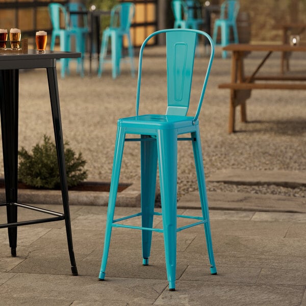 A turquoise Lancaster Table & Seating outdoor barstool on a sidewalk patio.