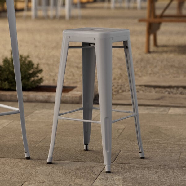 Two Lancaster Table & Seating nickel gray metal barstools on a stone surface.