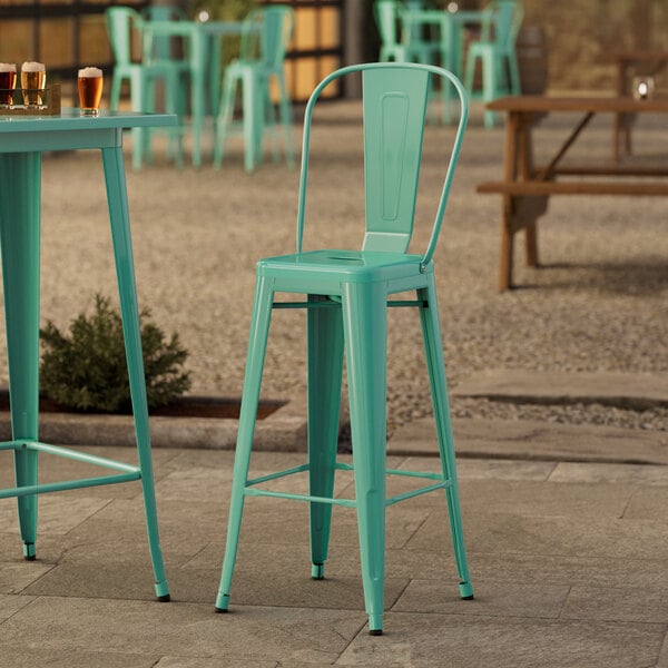 Three Lancaster Table & Seating aquamarine outdoor cafe barstools on an outdoor patio.