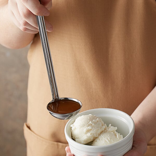 A person using a Vollrath stainless steel ladle to scoop ice cream into a bowl.