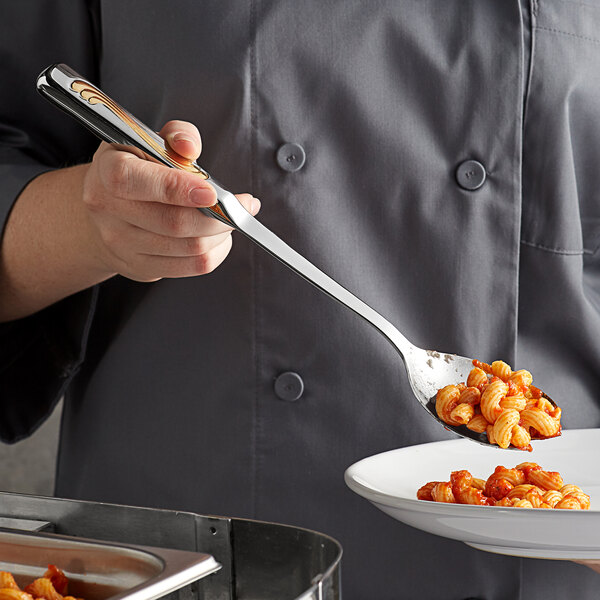 A person using a Vollrath Windway stainless steel notched serving spoon to serve pasta.