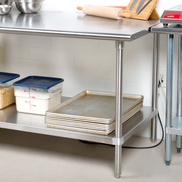 A stainless steel Advance Tabco work table with pans and bowls underneath.