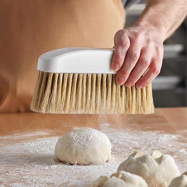 A hand holding an Ateco boar bristle bench brush over dough.