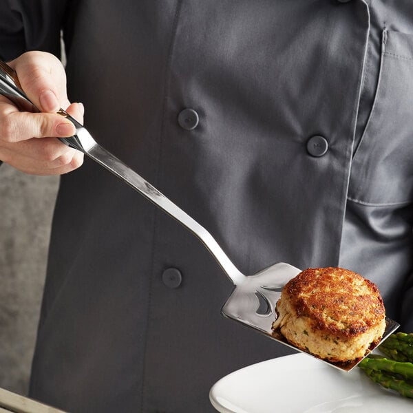 A person using a Vollrath stainless steel slotted turner to serve food.