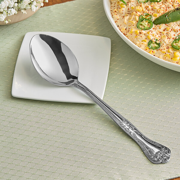 A Vollrath stainless steel serving spoon on a white plate with food.