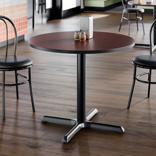A round laminated table with a reversible cherry and black top, supported by a black pedestal base.