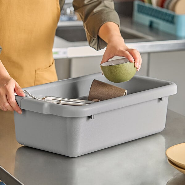 A woman using a Tablecraft grey undercounter bus tub to put a green bowl in.