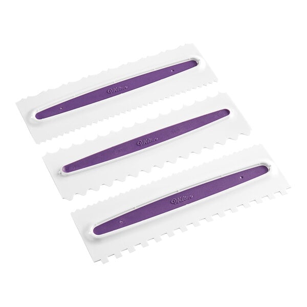 Three rectangular plastic decorating combs with purple handles and different notched edges, arranged side by side.