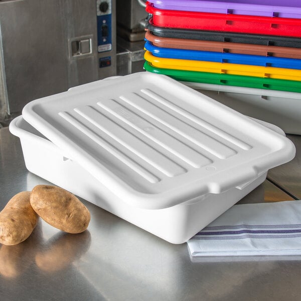 A white plastic Carlisle food storage container lid on a white plastic container filled with potatoes on a metal surface.