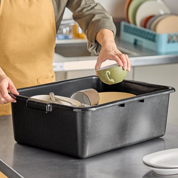 A woman putting dishes into a black Carlisle bus tub on a counter.