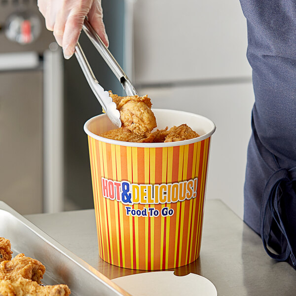 A person using tongs to pick up fried chicken from a Choice Hot Food Bucket.