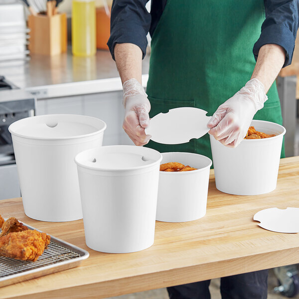 A person wearing gloves preparing food in a white Choice food bucket with a lid.