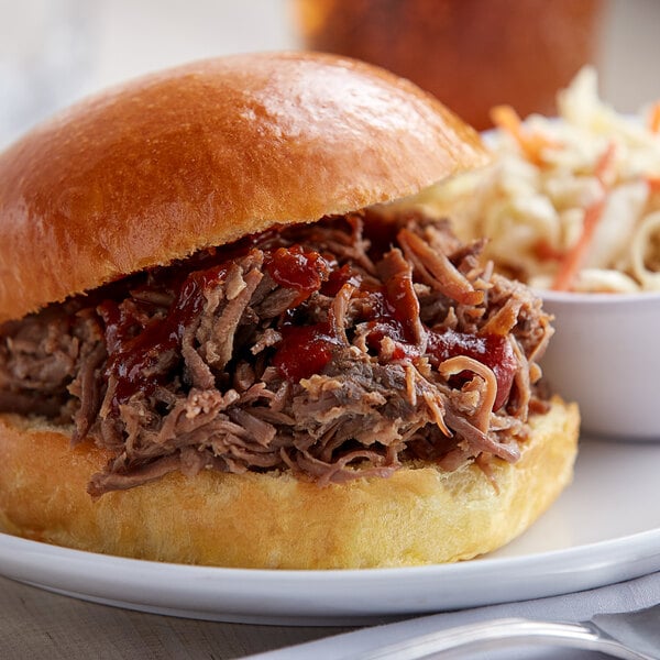 A pulled pork sandwich with coleslaw and a side of Cattlemen's Cowboy BBQ Rub on a plate.