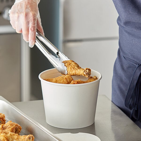 A person using tongs to put food in a Choice white food bucket.