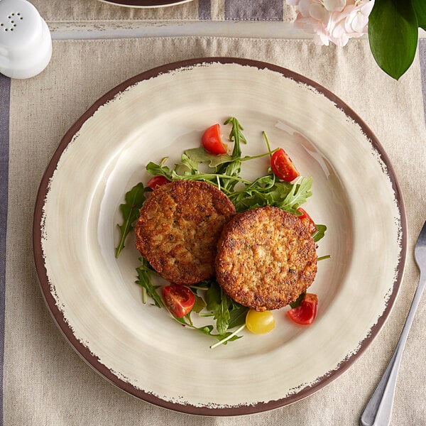 A Carlisle sweet cream melamine plate with two meat patties and salad on it.