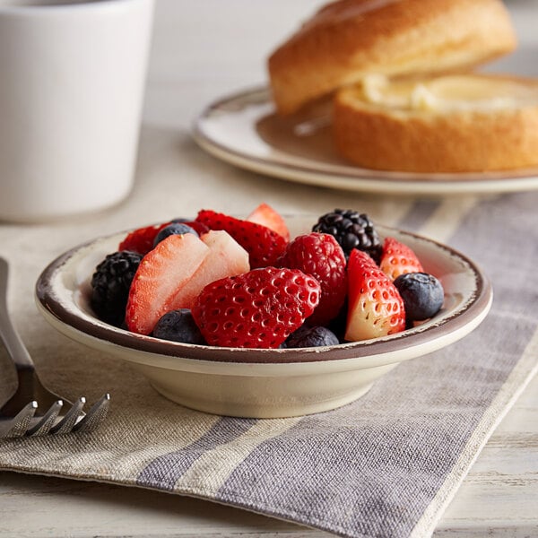 A Carlisle sweet cream melamine fruit bowl filled with fruit on a table with a white cup and spoon.