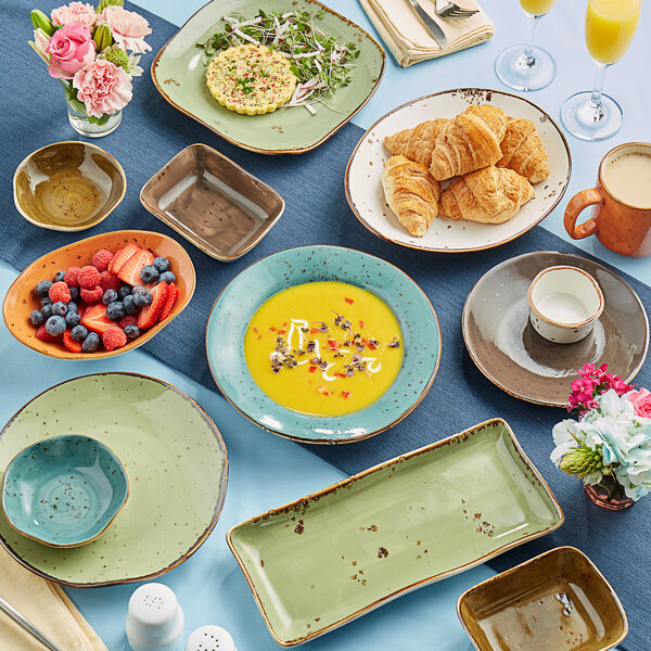 A white rectangular bowl with brown spots on a table with plates and food.