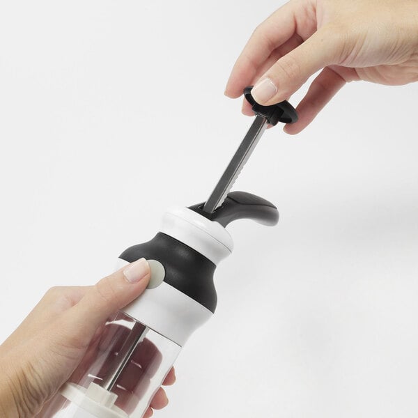 A hand holding a black OXO cookie press with a screwdriver.