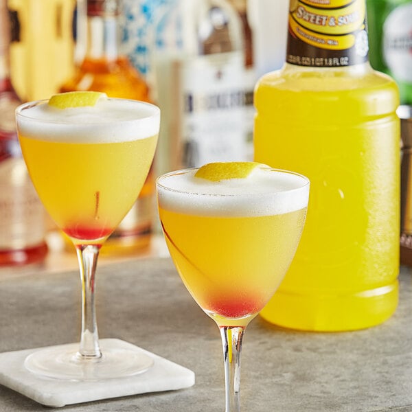 Two glasses of yellow liquid with lemon wedges on top on a table in a cocktail bar.