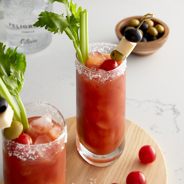A pair of Agalima Bloody Mary cocktails with celery and olives on a wooden board.