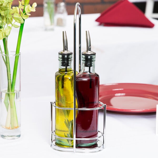 A Tablecraft Gemelli chrome rack holding a glass olive oil cruet and a glass vinegar cruet on a table.