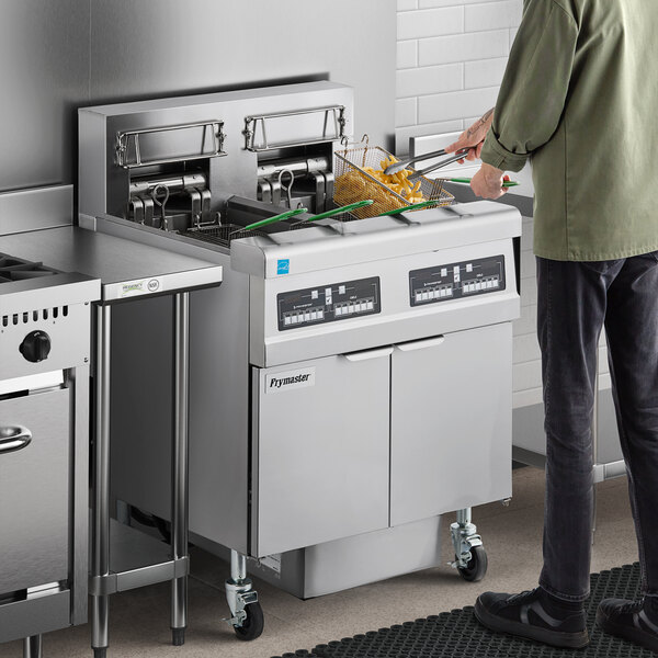 A man standing next to a Frymaster electric floor fryer with two open frypots.