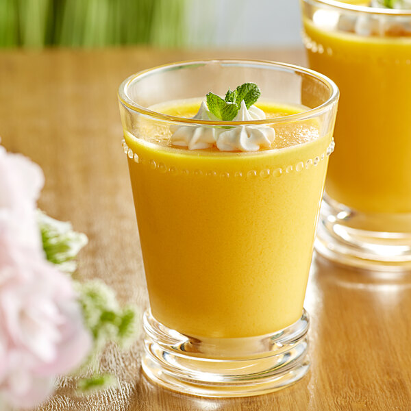 A glass of yellow mango pudding with whipped cream and mint leaves.