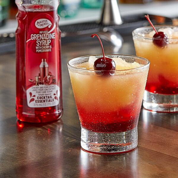 Two glasses of red drinks with Master of Mixes Grenadine Syrup and cherries on a counter.