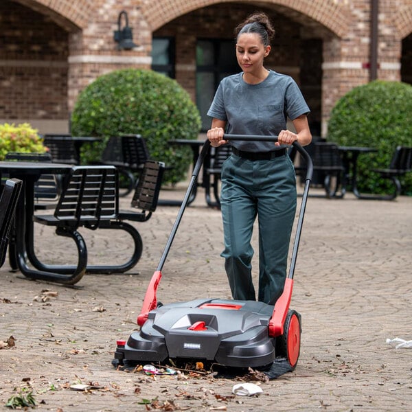 A battery powered triple brush power sweeper being used to clean outdoor debris.