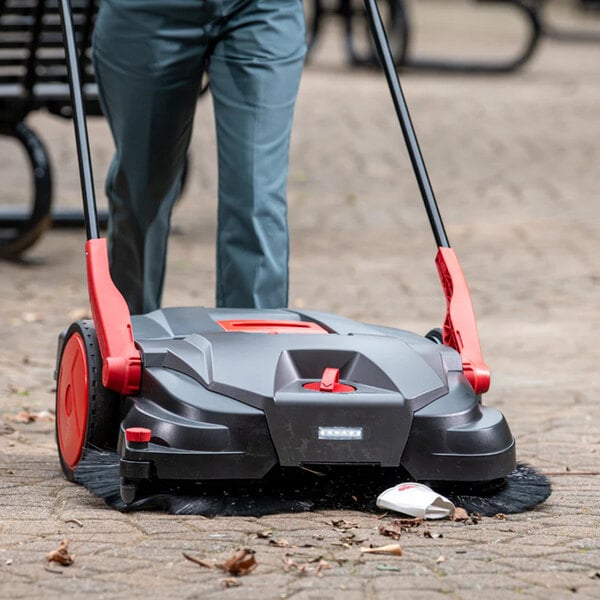 A battery powered triple brush power sweeper with a 31-inch cleaning path and 13.2 gallon capacity, being used on an outdoor surface.
