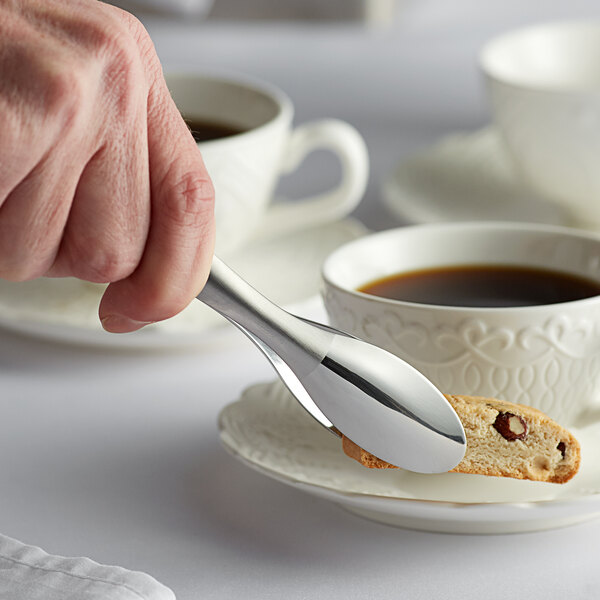 Stainless steel Tablecraft tongs being used to pick up a biscotti over a cup of coffee.