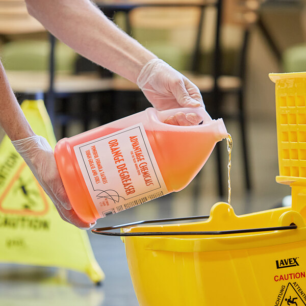 A hand pouring Advantage Chemicals orange degreaser into a yellow container.