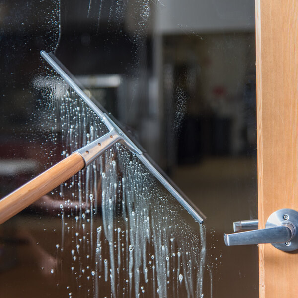 A 16-inch window squeegee with a steel handle being used to clean a glass door.