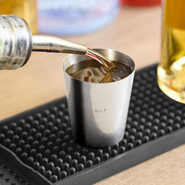A Franmara stainless steel shot glass on a table in a cocktail bar with liquid being poured into it.