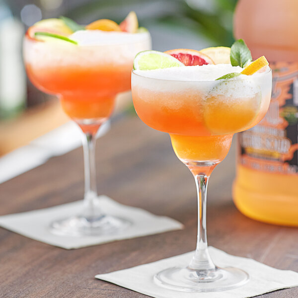 Two glasses of Finest Call Citrus Sour Mix on a table with garnished drinks.