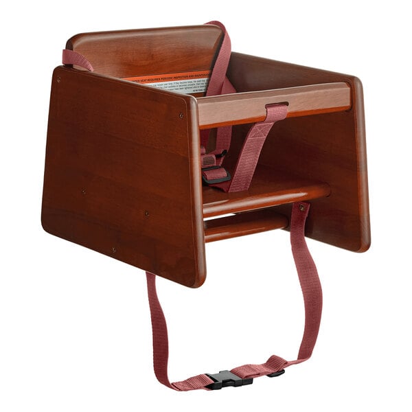 A wooden booster seat with a walnut finish, featuring a T-strap and safety harness.