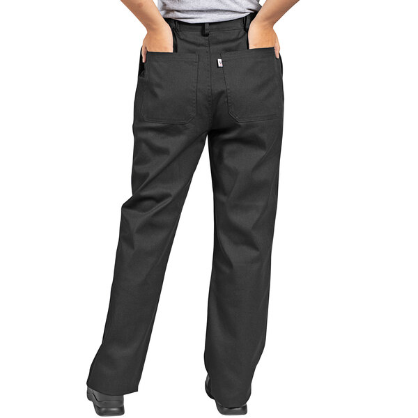 A person wearing Uncommon Chef black executive chef pants with their hands in their pockets.
