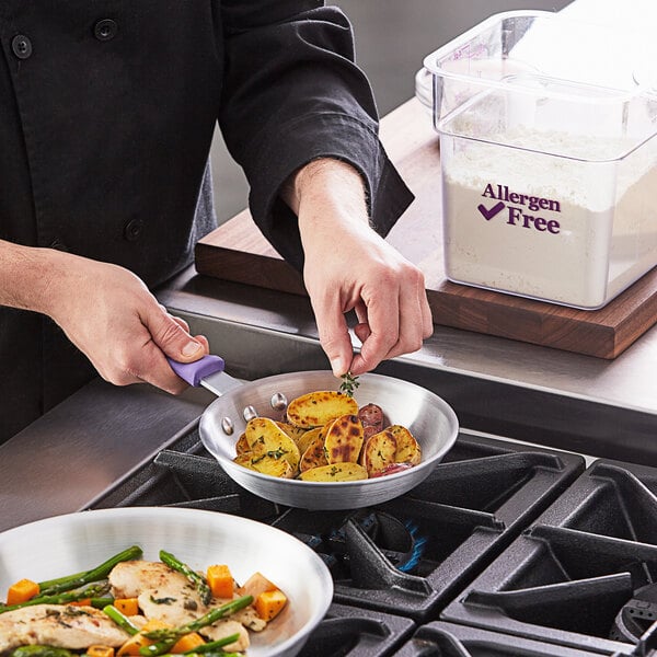 A person cooking food in a Choice aluminum fry pan with a purple allergen-free silicone handle.