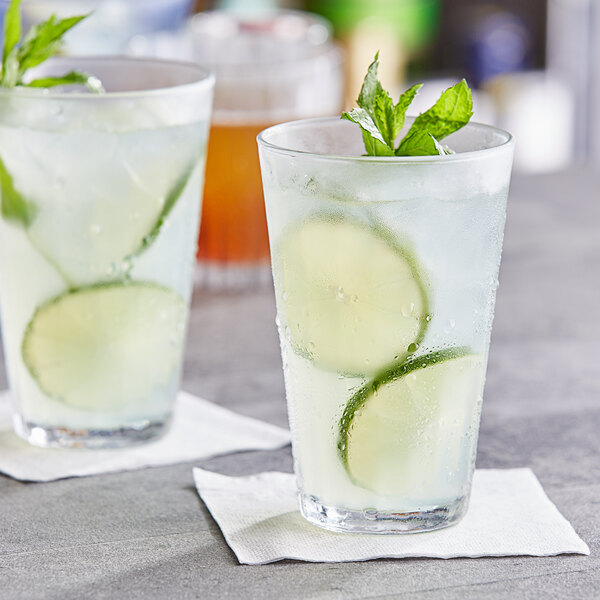 Two Duralex highball glasses of water with lime slices on a white background.