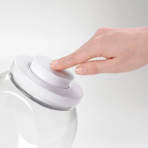 A hand pressing a white button on an OXO Good Grips plastic food storage container.