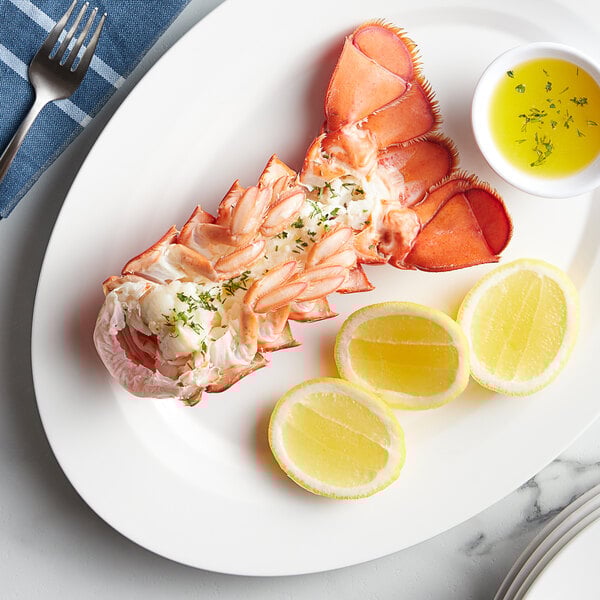 A Boston Lobster Company 10-12 oz. lobster tail on a plate with lemon slices and sauce.