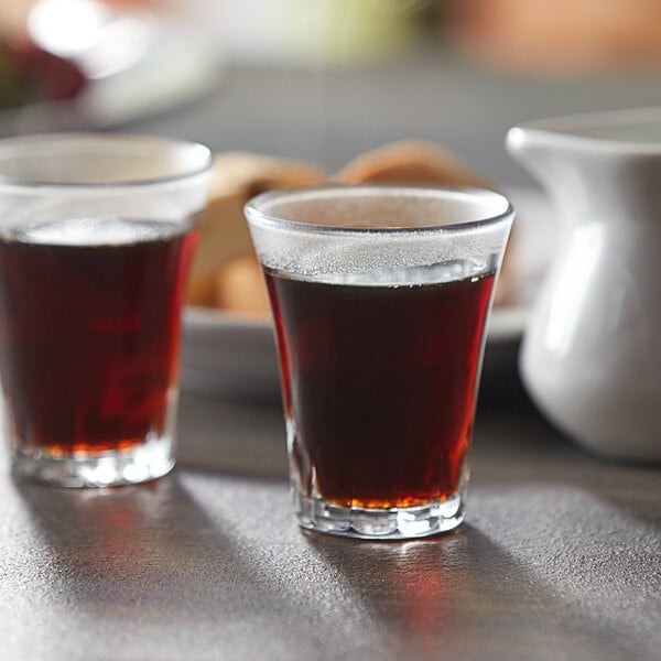 Two Duralex Amalfi espresso glasses filled with brown liquid on a table.