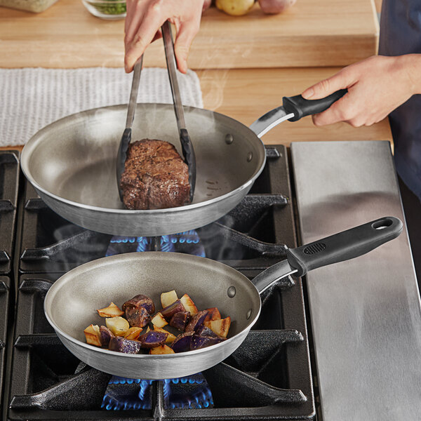 A person cooking meat in a Vollrath Wear-Ever non-stick fry pan on a stove.