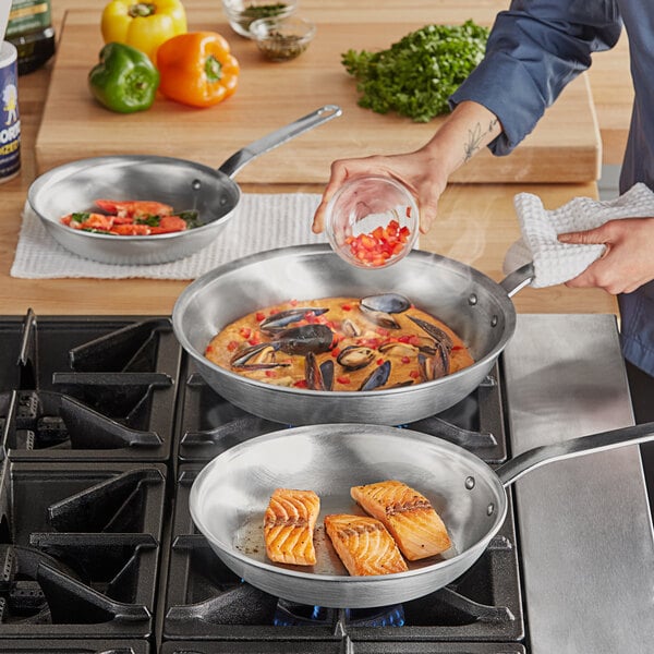 A woman pouring red peppers into a Vollrath Wear-Ever frying pan on a stove.